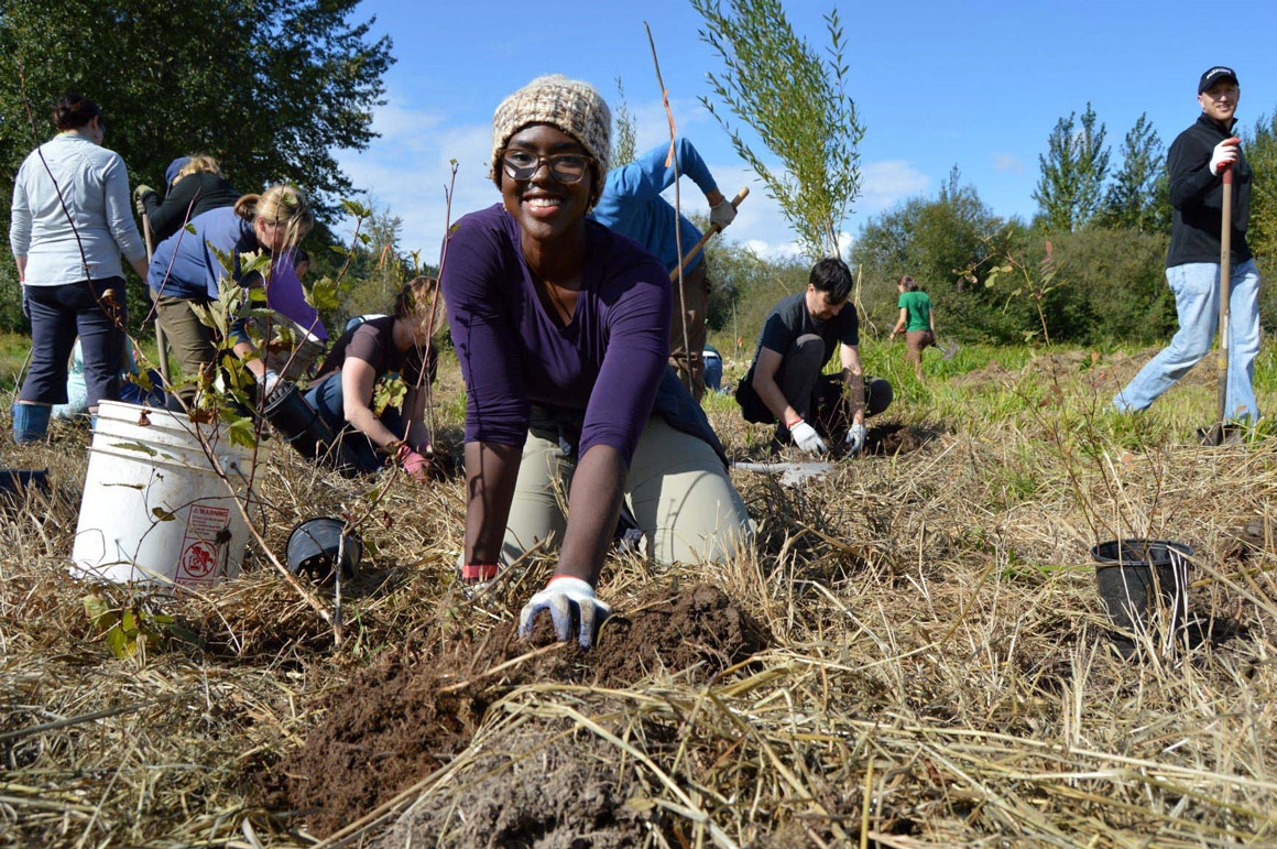 Young person in the foreground planting a tree at a restoration site