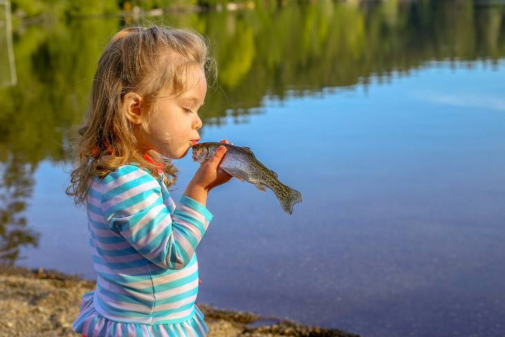 Child kissing a small trout with lake in the background.